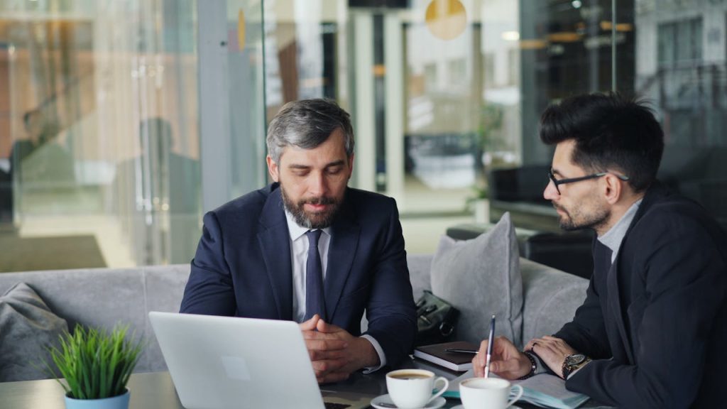 businessmen-talking-over-coffee-23496863 Two businessmen in suits discussing work at a cafe with laptops and coffee.
